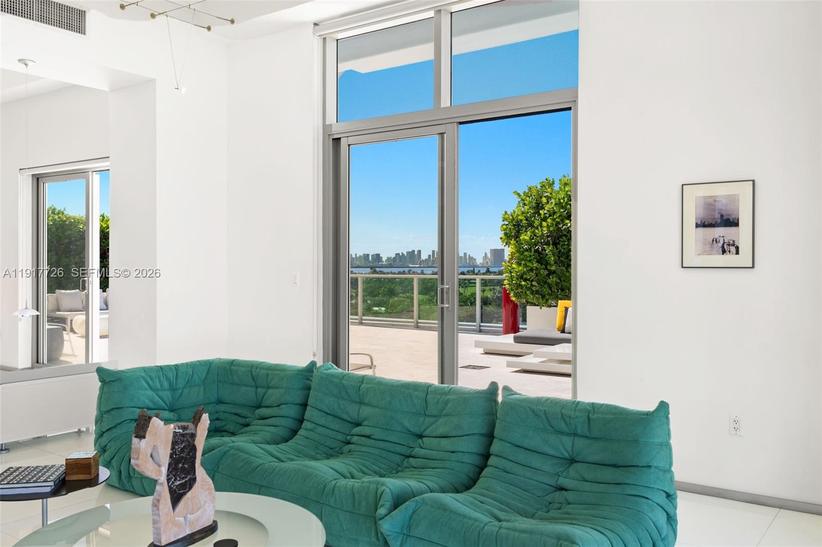 A living room features a teal tufted sofa, white walls, and sliding doors to a balcony — 201 Aqua Ave # 801, Miami Beach FL 33141, MIAMI BEACH, FL