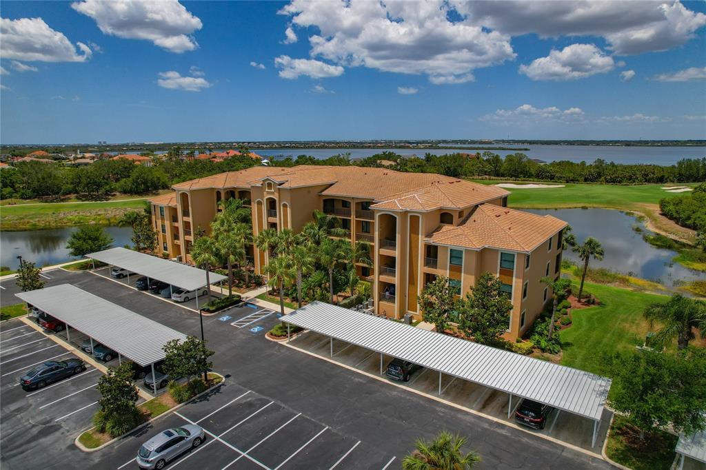 An aerial view shows a multi-story apartment building with covered parking and a surrounding golf course — 6411 GRAND ESTUARY TRAIL UNIT 401, BRADENTON, FL