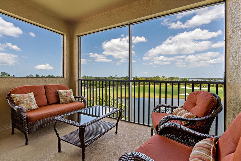 A screened-in balcony features wicker furniture and a view of a golf course and lake — 6411 GRAND ESTUARY TRAIL UNIT 401, BRADENTON, FL