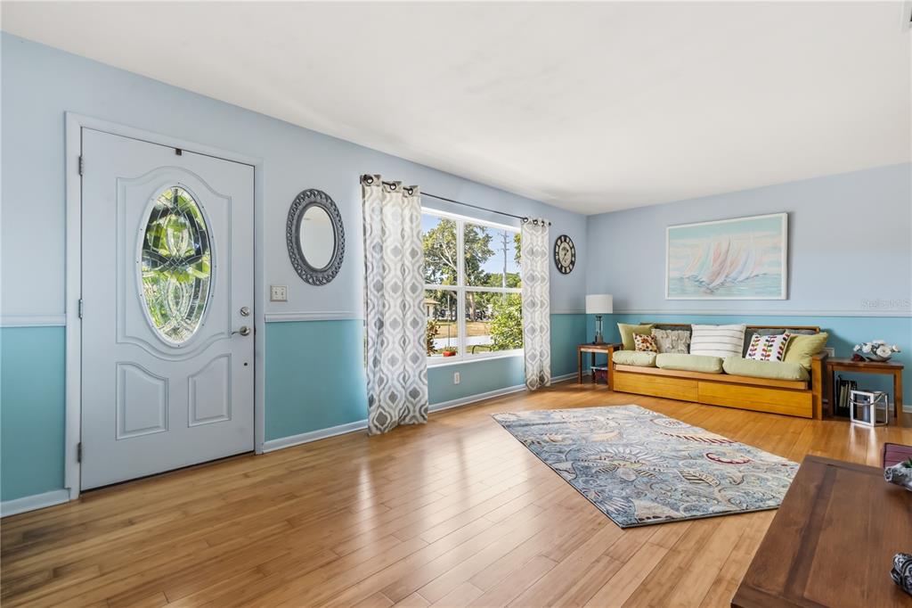 A living room with light blue walls, hardwood floors, a front door, and a sofa — 1508 ERIN LANE, CLEARWATER, FL