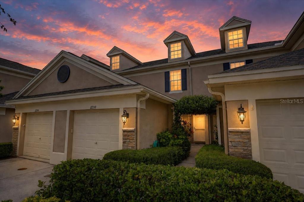 A multi-unit residential building exterior features three garage doors, dormer windows, and a sunset sky — 11208 WINDSOR PLACE CIRCLE, TAMPA, FL