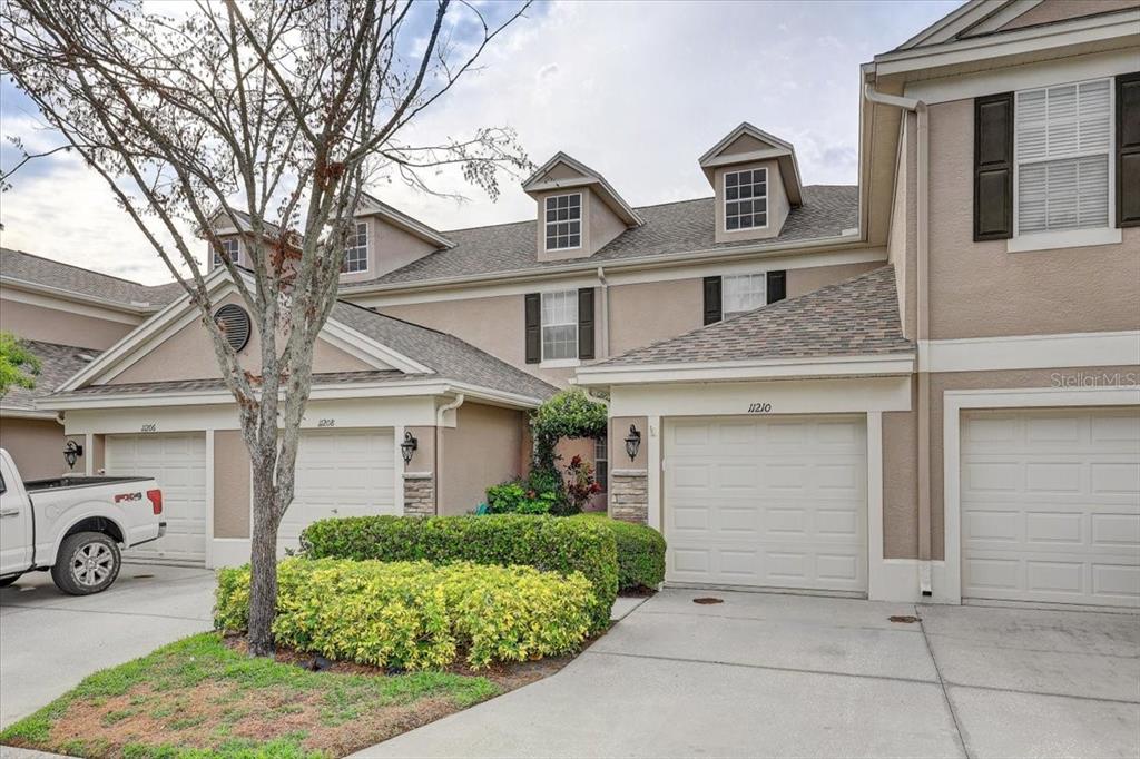 A multi-unit residential building with beige stucco siding, gabled roofs, and attached garage doors — 11208 WINDSOR PLACE CIRCLE, TAMPA, FL