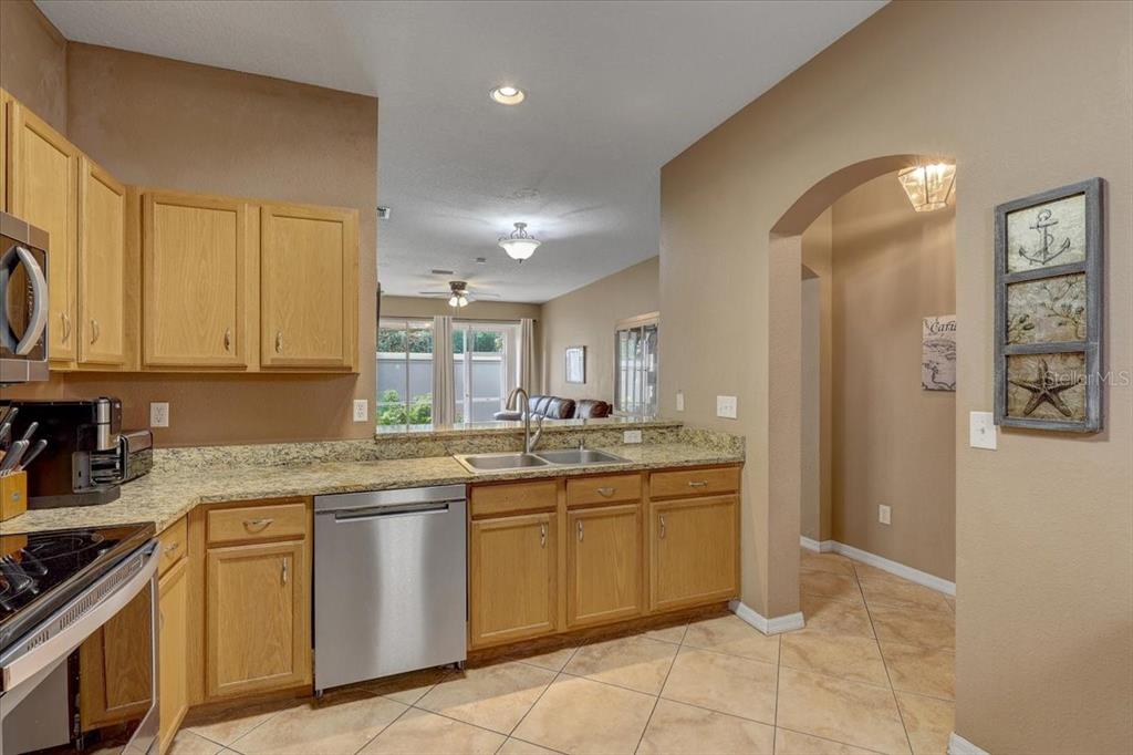 A kitchen features light wood cabinets, granite countertops, stainless steel appliances, and tile flooring — 11208 WINDSOR PLACE CIRCLE, TAMPA, FL
