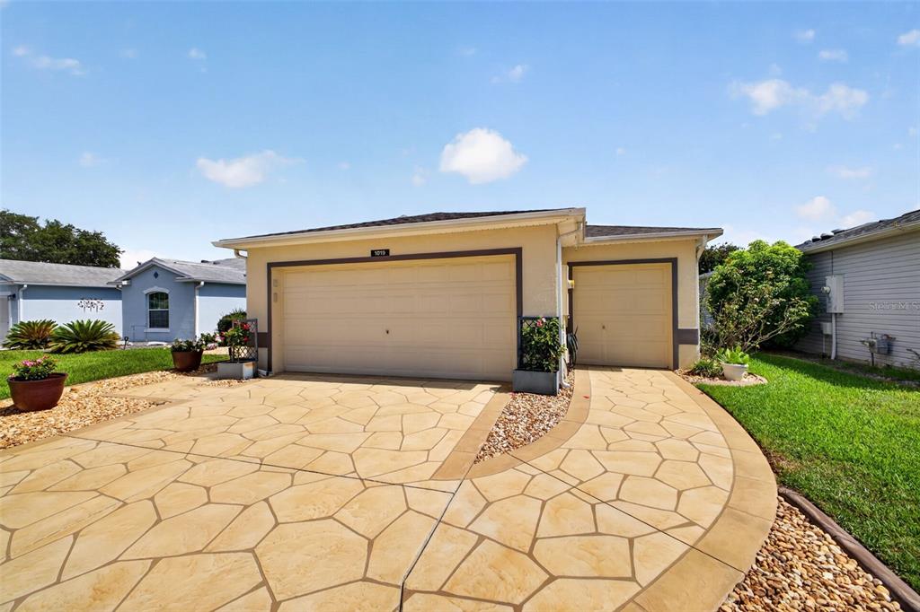 A single-story house exterior features a two-car garage, a paved driveway, and landscaped front yards — 1019 EAGLES LANDING, LEESBURG, FL