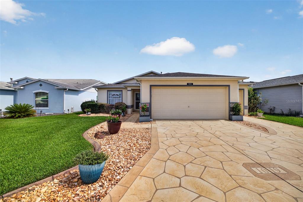 A single-story house with a beige stucco exterior, a two-car garage, and a stone-patterned driveway — 1019 EAGLES LANDING, LEESBURG, FL