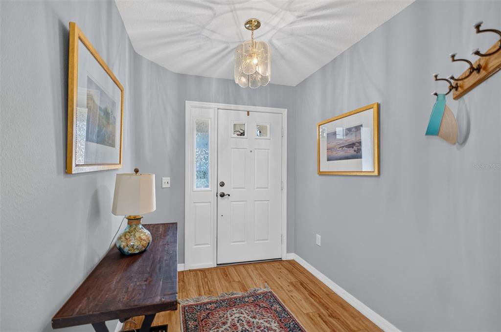 An entryway features a white front door, wood flooring, a console table, and wall art — 1019 EAGLES LANDING, LEESBURG, FL