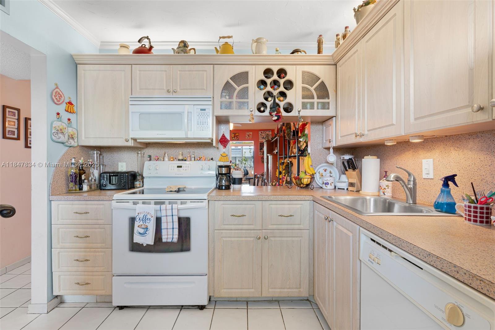 A kitchen features light wood cabinets, white appliances, a tiled floor, and a pass-through window — 3120 Holiday Springs Blvd # 301, Margate FL 33063, MARGATE, FL