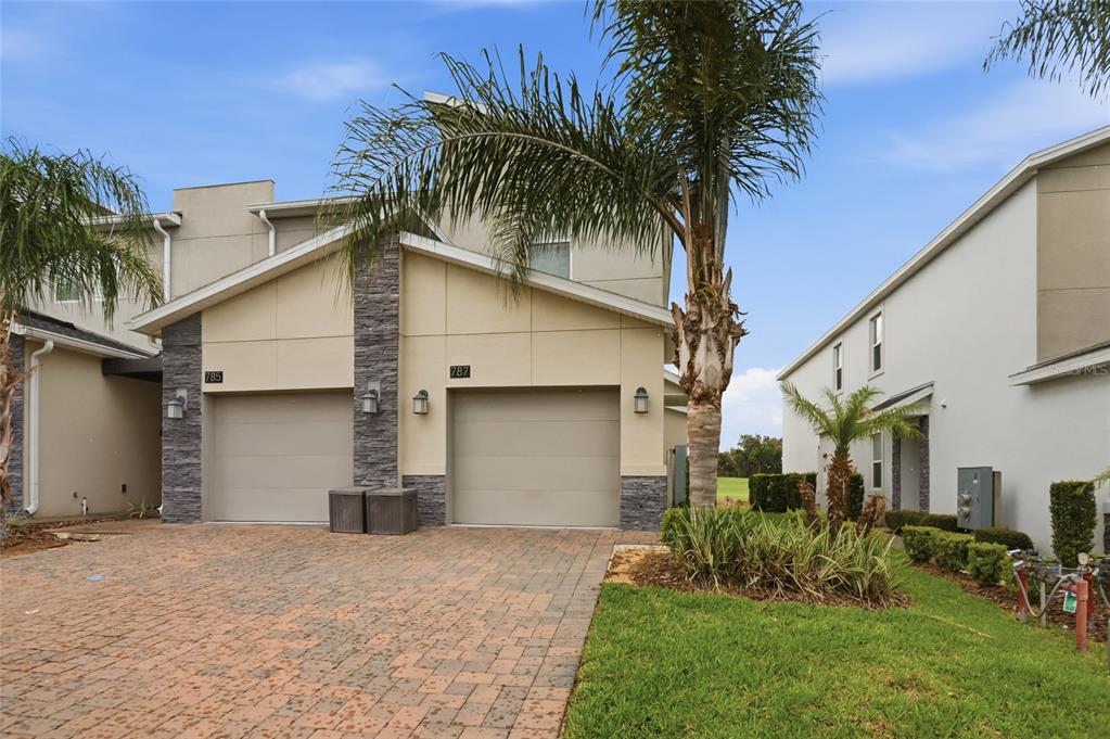 A two-story townhouse with a stone-accented facade, two garage doors, and a paved driveway — 787 OCEAN COURSE AVENUE, KISSIMMEE, FL