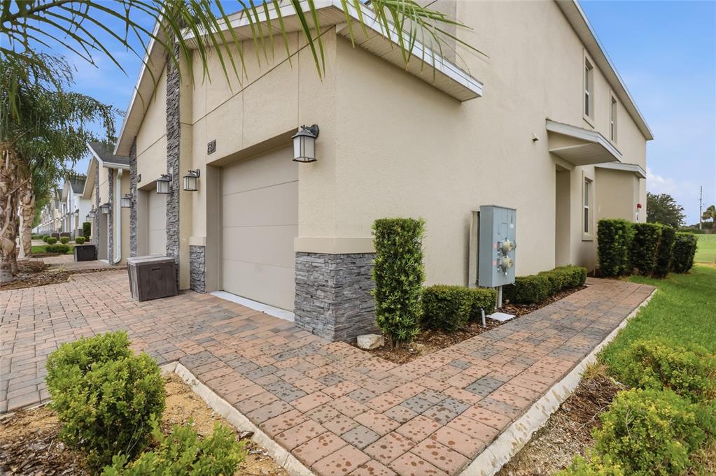 The exterior of a beige townhouse featuring a garage, stone accents, and a paved walkway — 787 OCEAN COURSE AVENUE, KISSIMMEE, FL