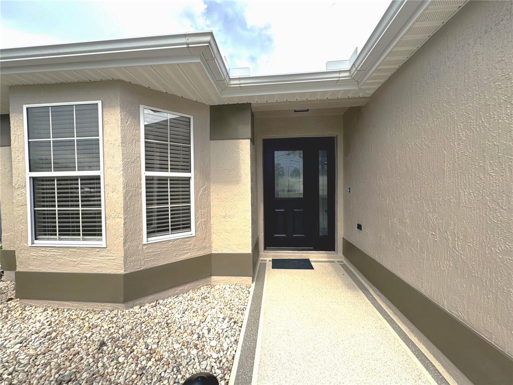 A beige stucco house exterior features a black front door and a gravel garden bed — 2264 MARGARITA DRIVE, THE VILLAGES, FL