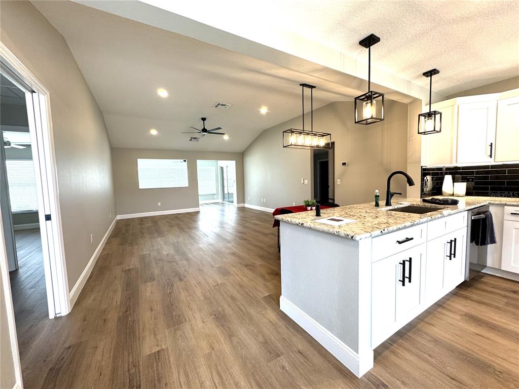 A kitchen island with granite countertops sits in an open-concept living area with wood flooring — 2264 MARGARITA DRIVE, THE VILLAGES, FL
