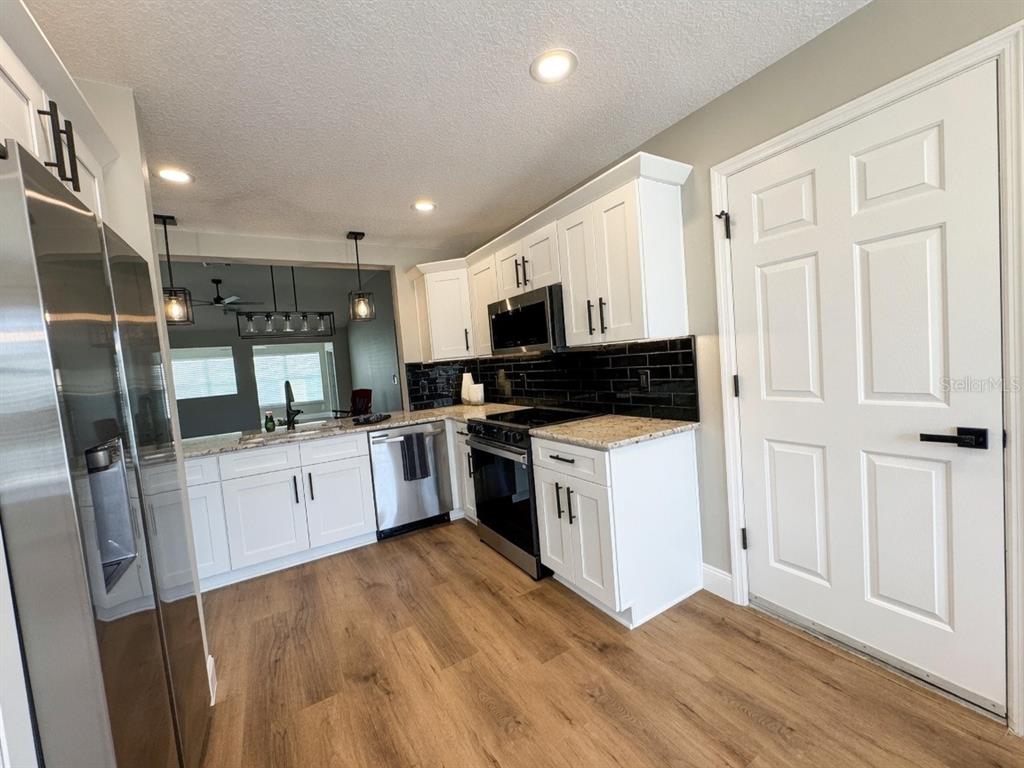 A kitchen features white cabinets, black subway tile backsplash, granite countertops, and wood-look flooring — 2264 MARGARITA DRIVE, THE VILLAGES, FL