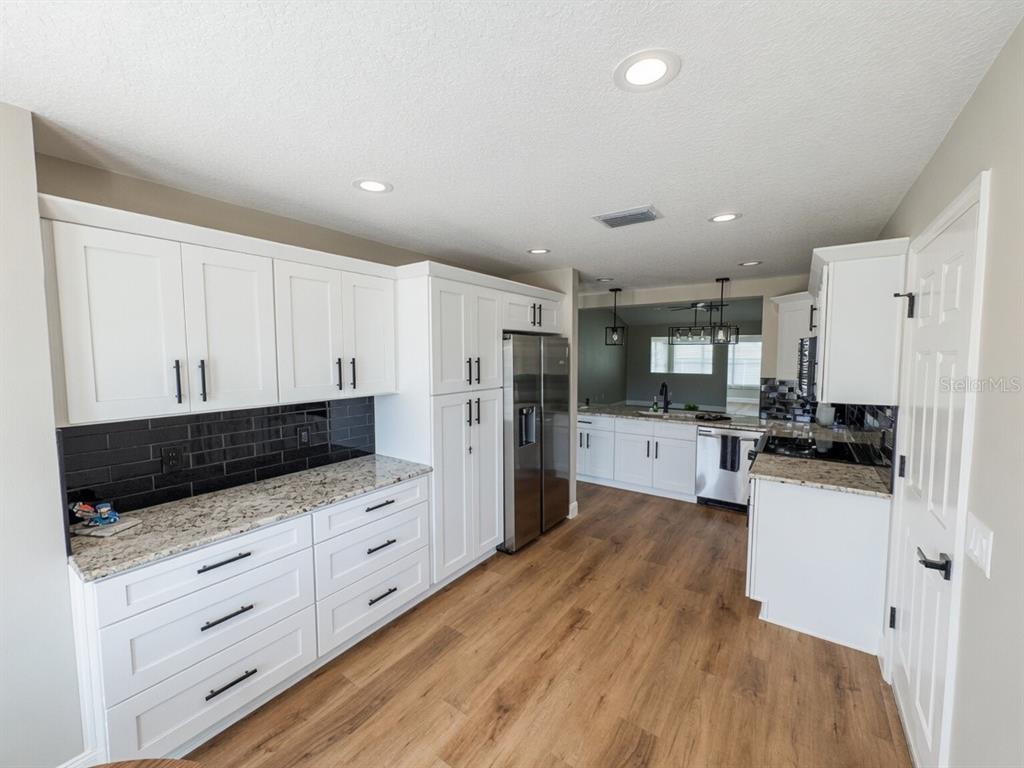 A kitchen features white cabinets, granite countertops, a black subway tile backsplash, and wood flooring — 2264 MARGARITA DRIVE, THE VILLAGES, FL