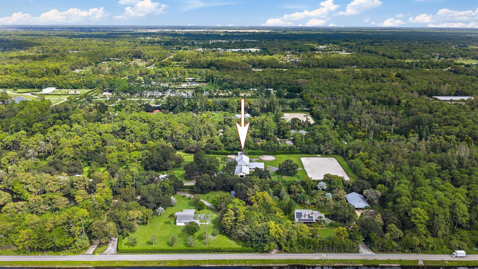 An aerial view shows a rural property with a house, stables, and a riding arena — 14339 Collecting Canal Road, FL 33470, FL