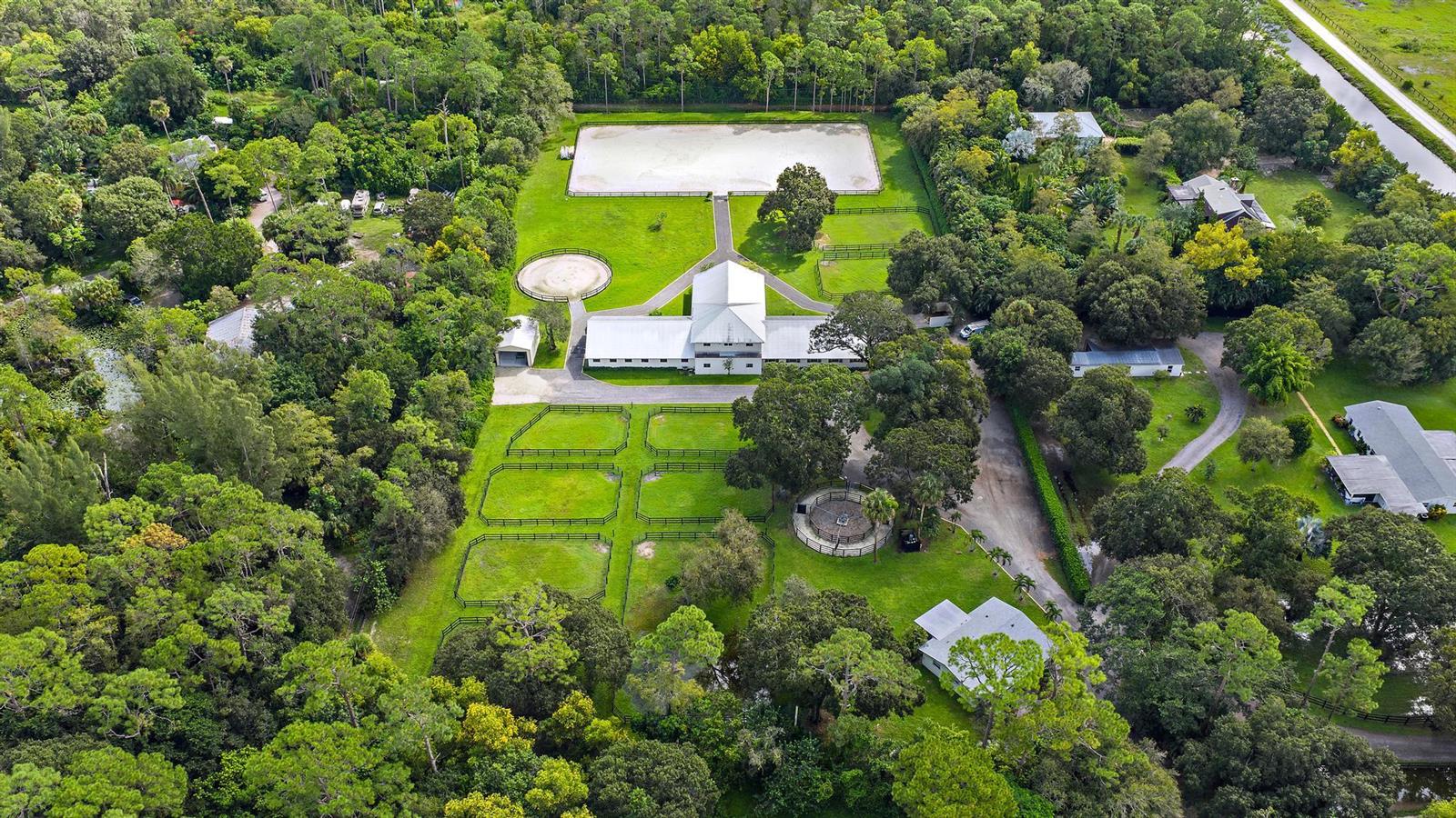 An aerial view of a horse property featuring a barn, riding arena, and fenced paddocks — 14339 Collecting Canal Road, FL 33470, FL