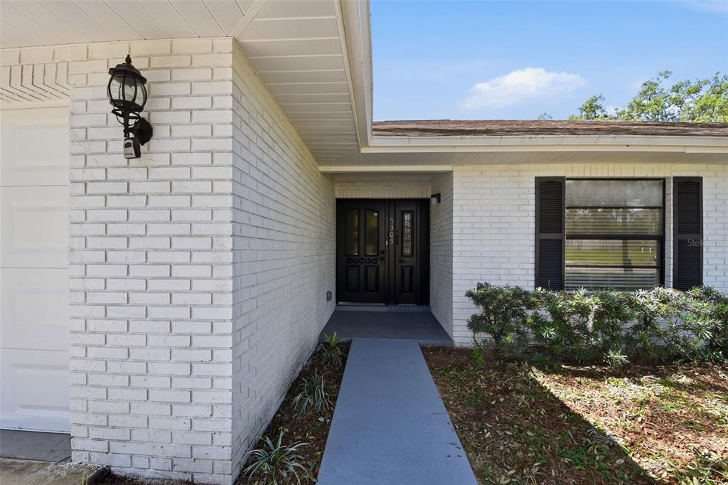 A white brick house exterior features a black double front door and a concrete walkway — 5305 E 127TH AVENUE, TAMPA, FL