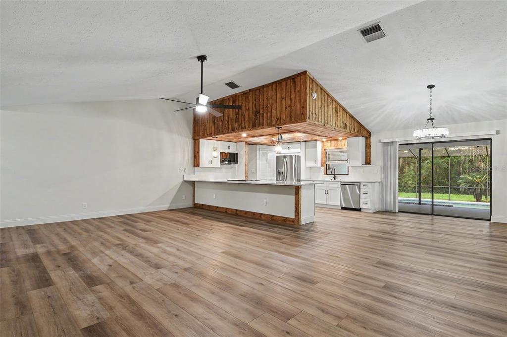 A spacious living room with wood-look flooring opens to a kitchen featuring wood-paneled ceiling accents — 5305 E 127TH AVENUE, TAMPA, FL