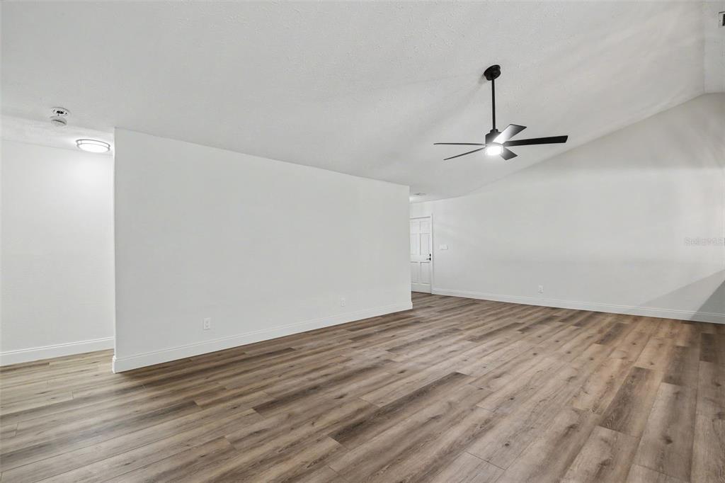 An empty room features white walls, a vaulted ceiling with a ceiling fan, and wood-look flooring — 5305 E 127TH AVENUE, TAMPA, FL