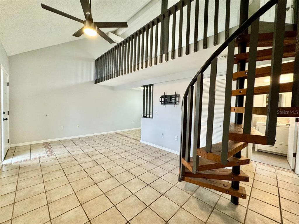 A room with tiled floors, a spiral staircase, and a loft area with a railing — 2166 BRADFORD STREET UNIT 125, CLEARWATER, FL