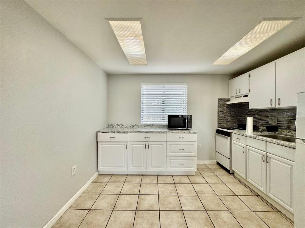 A kitchen features white cabinets, granite countertops, a tiled backsplash, and light-colored floor tiles — 2166 BRADFORD STREET UNIT 125, CLEARWATER, FL