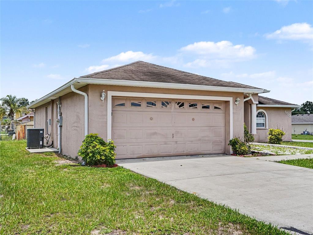 A tan house exterior features a two-car garage, a concrete driveway, and a grassy yard — 1802 HUDSON COURT, KISSIMMEE, FL