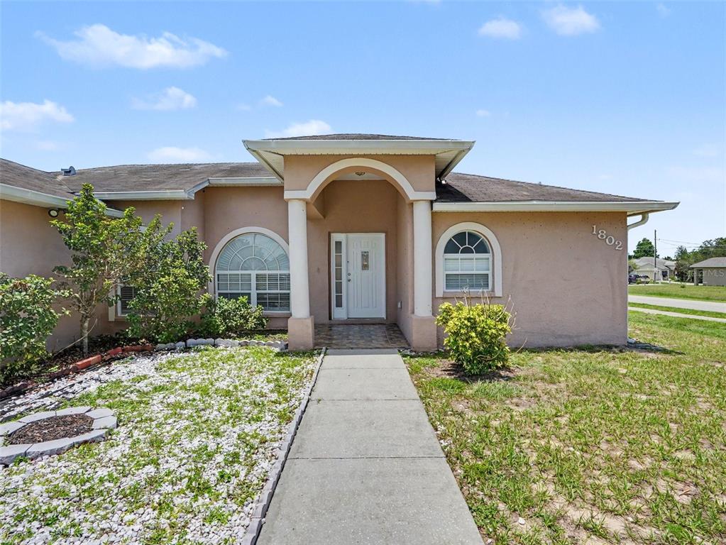 A single-story house with a beige stucco exterior, arched windows, and a covered front entrance — 1802 HUDSON COURT, KISSIMMEE, FL
