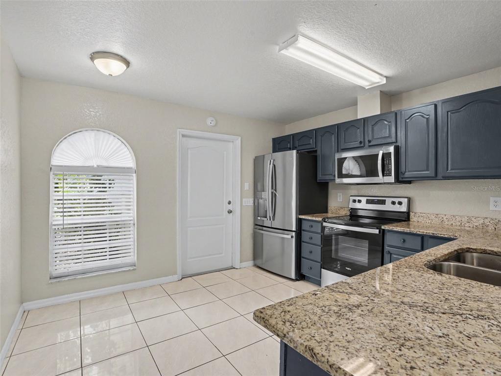 A kitchen features dark blue cabinets, granite countertops, stainless steel appliances, and tile flooring — 1802 HUDSON COURT, KISSIMMEE, FL