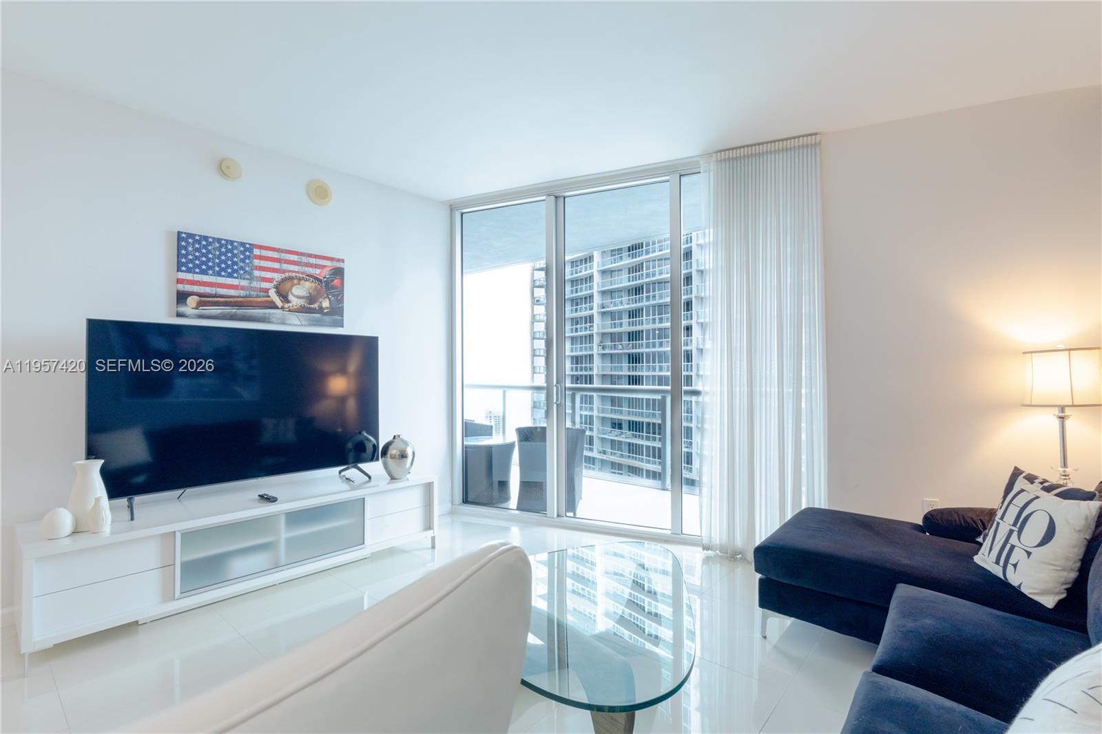 A modern living room features a large television, white media console, and a dark sofa — 475 Brickell Ave # 4511, Miami FL 33131, MIAMI, FL