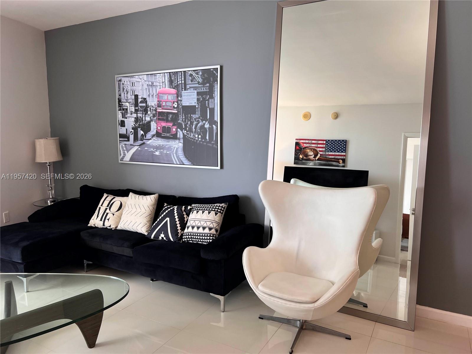 A modern living room features a black sectional sofa, a white egg chair, and a mirror — 475 Brickell Ave # 4511, Miami FL 33131, MIAMI, FL