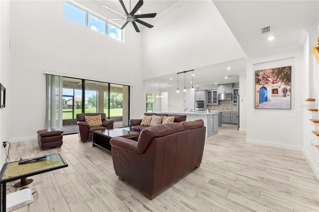A spacious living room with high ceilings, wood-look tile floors, and an open-concept kitchen — 1100 WINDLASS COURT, KISSIMMEE, FL