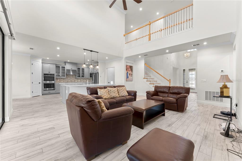 An open-concept living room and kitchen featuring light wood-look tile floors and leather furniture — 1100 WINDLASS COURT, KISSIMMEE, FL