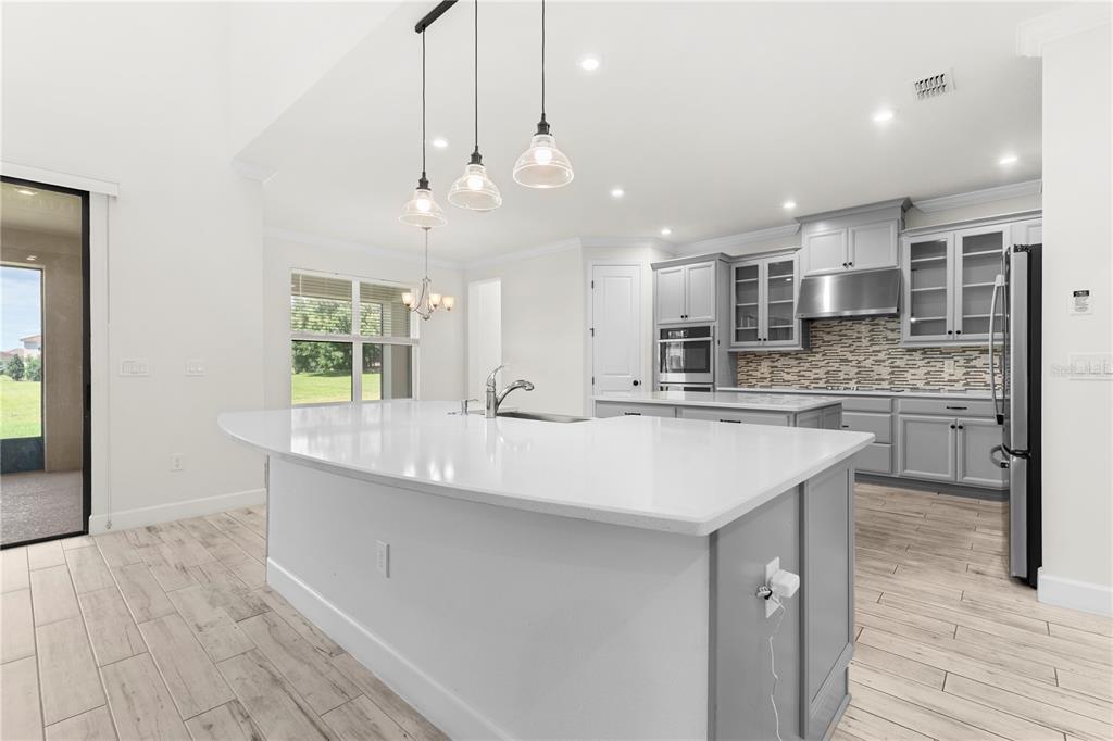 A modern kitchen features a large white island, grey cabinetry, and light wood-look tile flooring — 1100 WINDLASS COURT, KISSIMMEE, FL