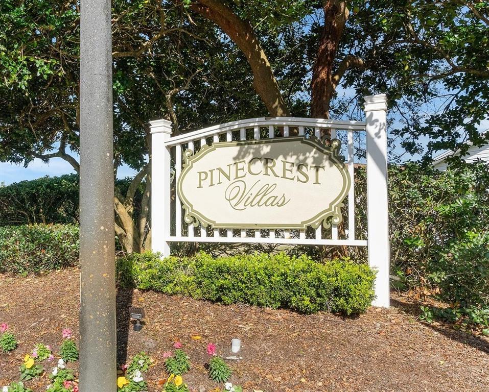 A white sign with the text Pinecrest Villas stands in front of trees and bushes — 17470 SE 93RD VINE AVENUE, THE VILLAGES, FL