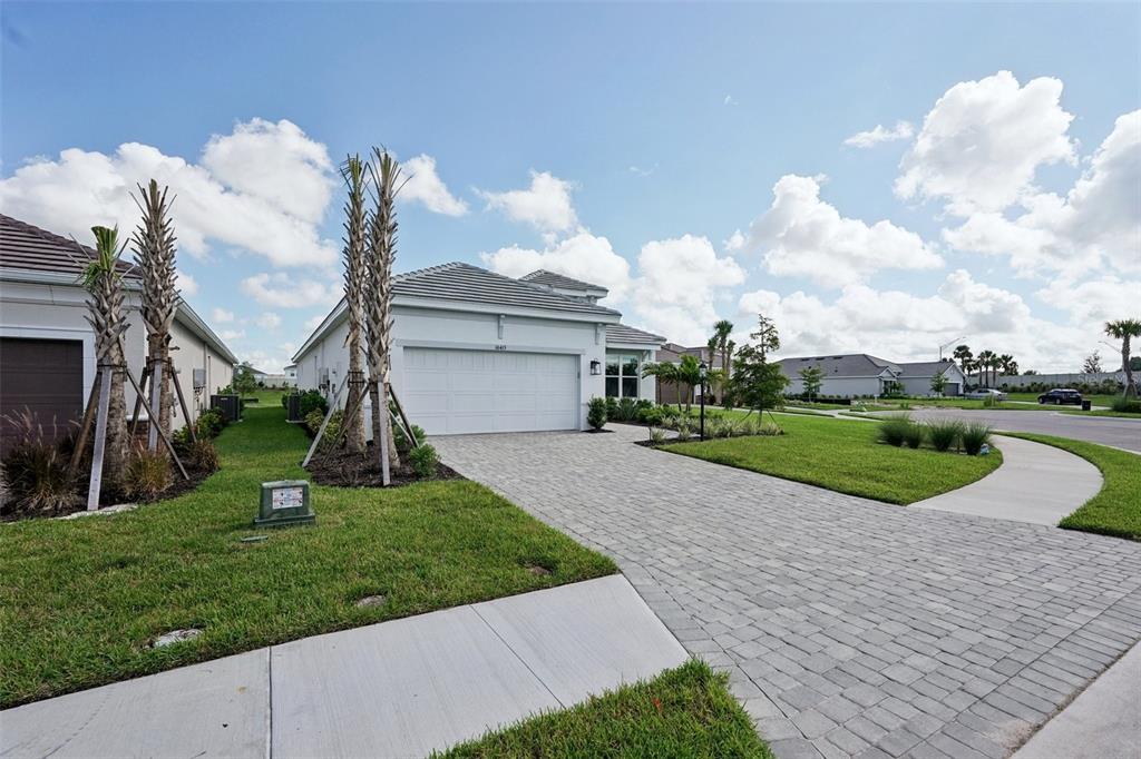 A single-story house with a white garage, paver driveway, and palm trees in the front yard — 16415 ISOLA PLACE, LAKEWOOD RANCH, FL