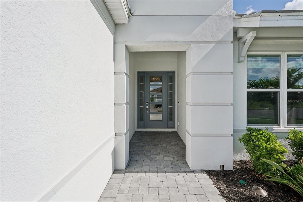 A paved walkway leads to a gray front door recessed within a white stucco entryway — 16415 ISOLA PLACE, LAKEWOOD RANCH, FL