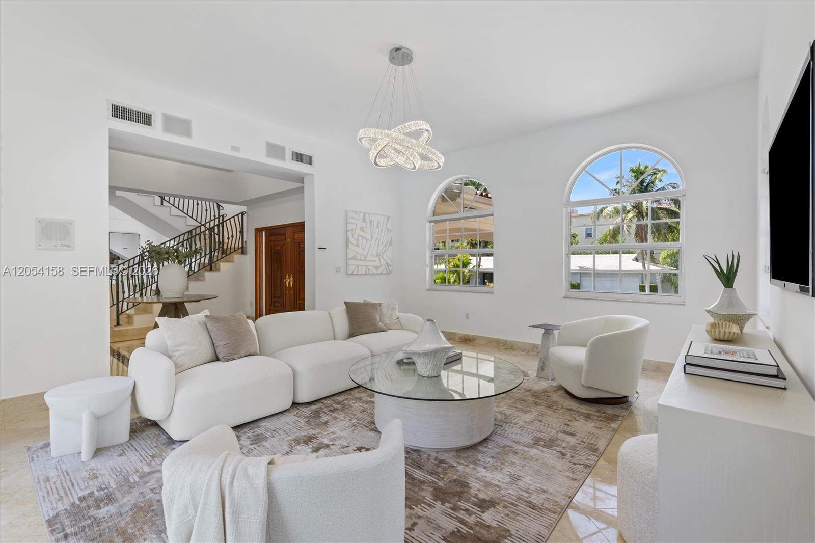 A bright living room features a white sectional sofa, arched windows, and a modern chandelier — 145 W Sunrise Ave, Coral Gables FL 33133, CORAL GABLES, FL