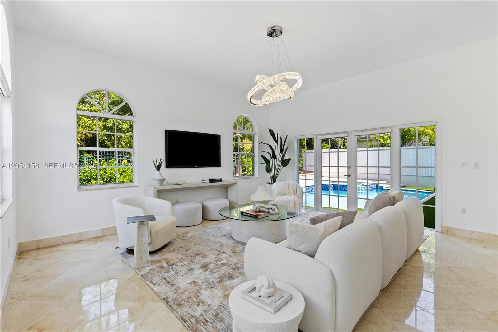 A bright living room features white furniture, a glass coffee table, and a pool view — 145 W Sunrise Ave, Coral Gables FL 33133, CORAL GABLES, FL