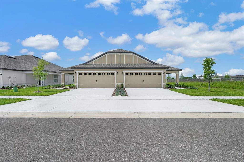 A single-story duplex with two tan garage doors and a shared concrete driveway — 3176 SEVILLE STREET, LAKE ALFRED, FL