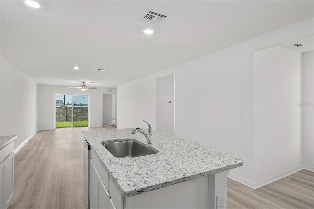A kitchen island with a granite countertop and sink overlooks an open-concept living area — 3176 SEVILLE STREET, LAKE ALFRED, FL