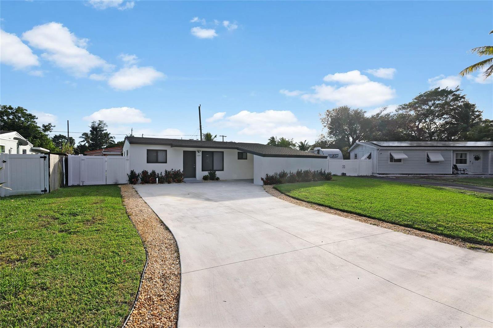 A single-story house with a concrete driveway and white vinyl fencing under a blue sky — 6374 SW 2nd Street, Margate FL 33068, MARGATE, FL