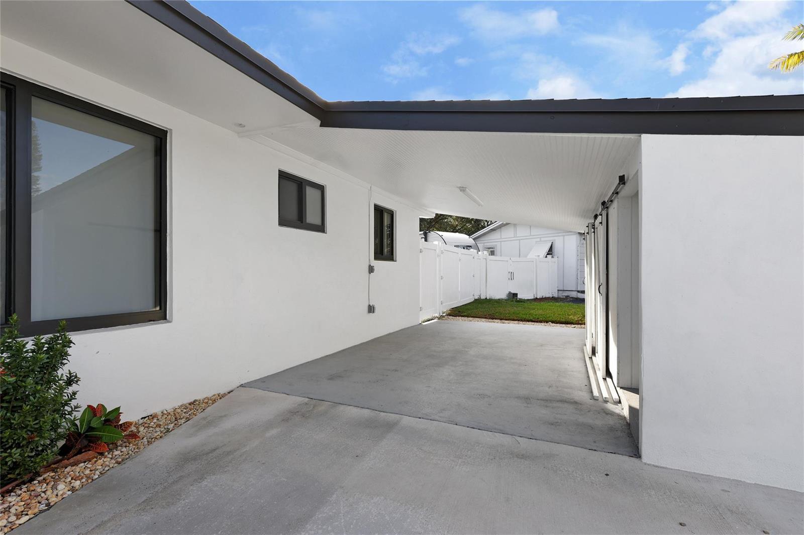 A concrete carport with a white ceiling and sliding doors attached to a white house — 6374 SW 2nd Street, Margate FL 33068, MARGATE, FL