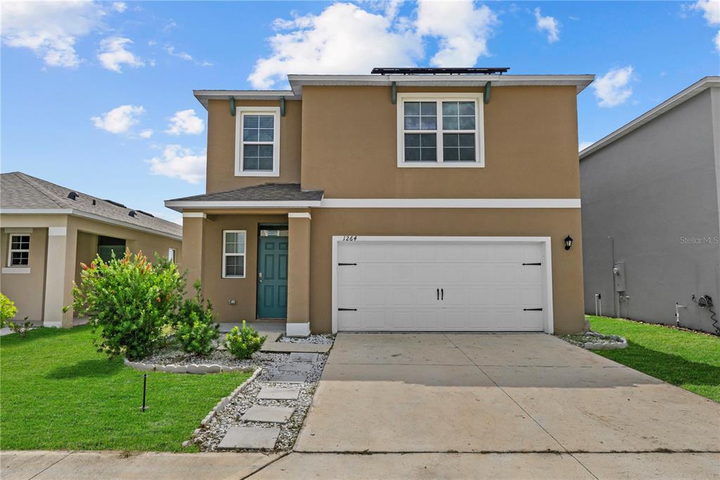 A two-story house with a tan stucco exterior, a white garage door, and a front lawn — 1264 CASCADES AVENUE, DAVENPORT, FL