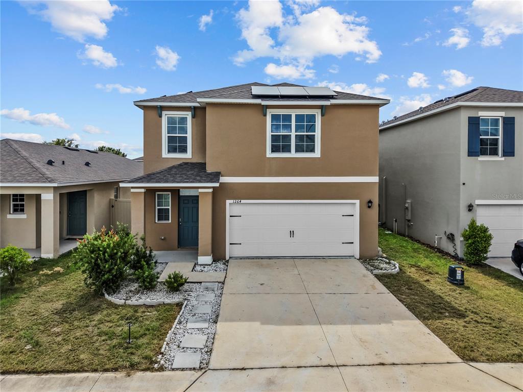 A two-story tan house features a two-car garage, a front walkway, and solar panels — 1264 CASCADES AVENUE, DAVENPORT, FL