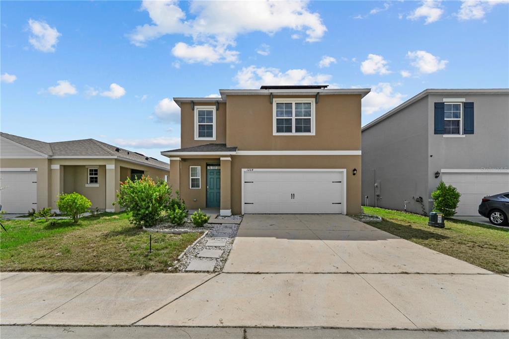 A two-story tan house with a white garage door and a concrete driveway — 1264 CASCADES AVENUE, DAVENPORT, FL