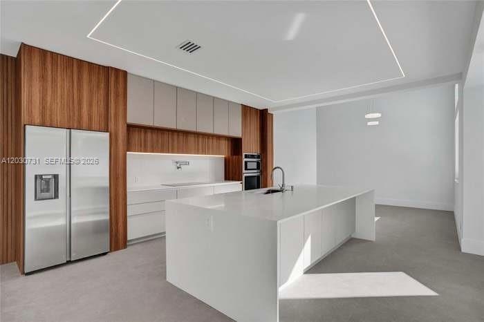 A modern kitchen features a large white island, stainless steel refrigerator, and wood-paneled cabinetry — 852 Heritage Dr, Weston FL 33326, WESTON, FL