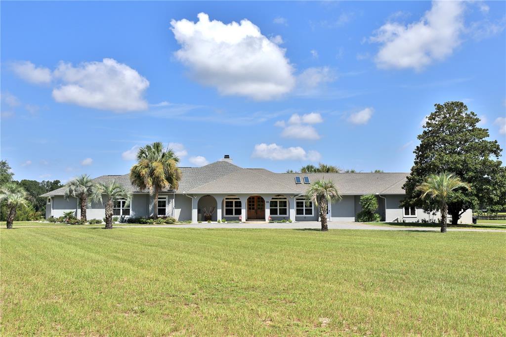 A wide, single-story gray house with a large lawn and several palm trees — 14285 N US HIGHWAY 441, CITRA, FL