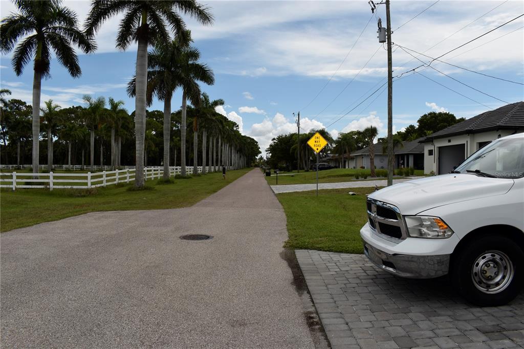 A paved road lined with palm trees and a white fence next to a parked truck — 805 SW 6TH COURT, CAPE CORAL, FL