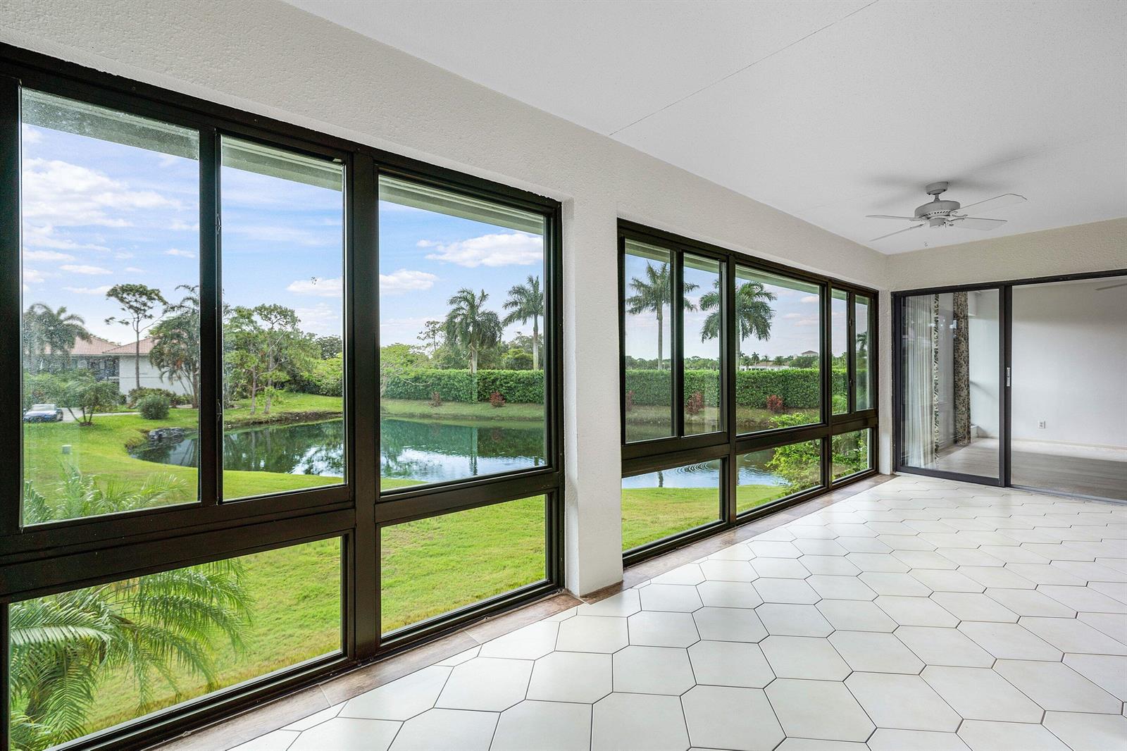 A sunroom with white hexagonal floor tiles, large windows overlooking a pond, and a ceiling fan — 4080-b Quail Ridge Drive, Boynton Beach FL 33436, BOYNTON BEACH, FL