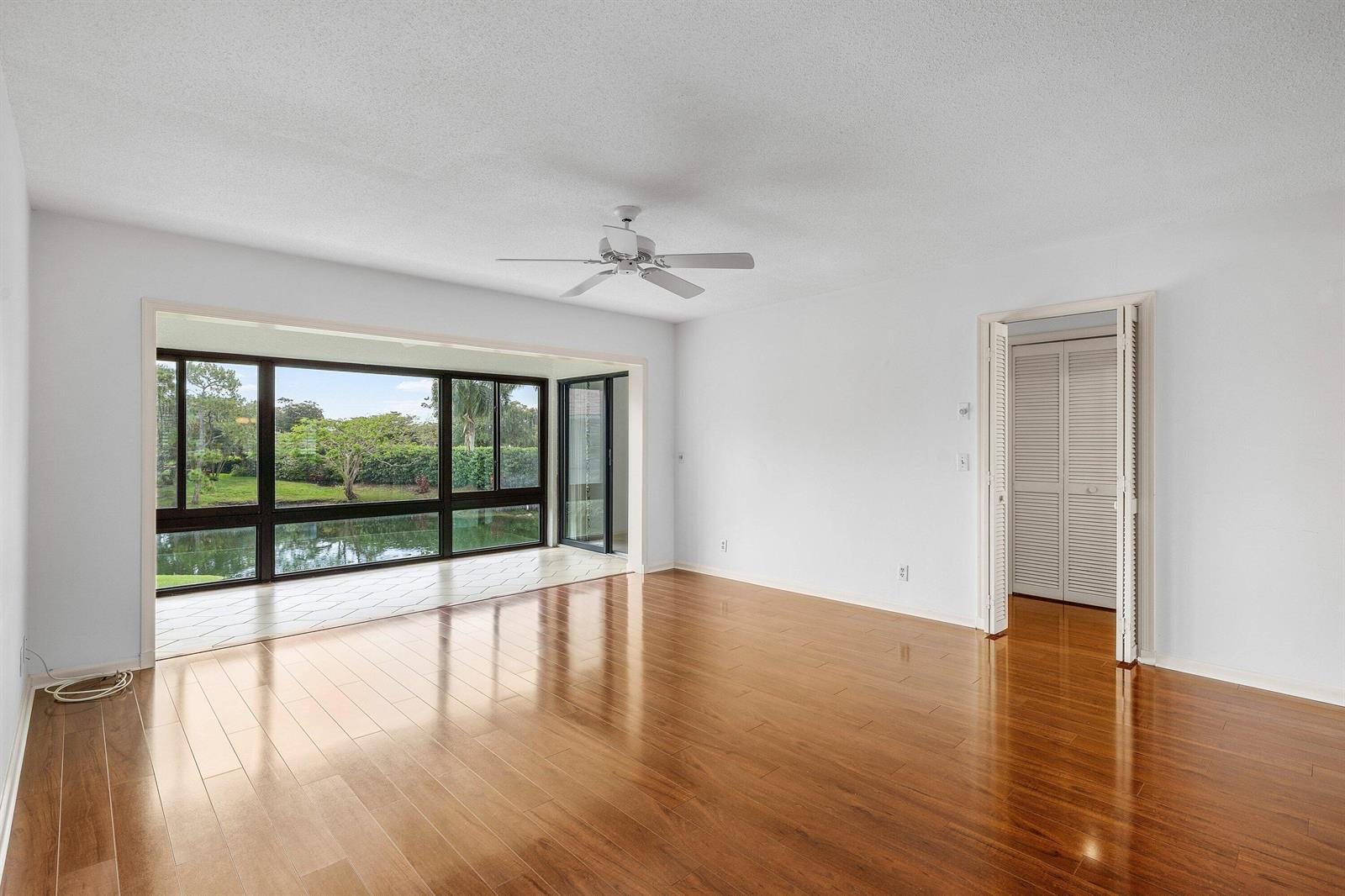 An empty living room features hardwood floors, a ceiling fan, and large windows overlooking water — 4080-b Quail Ridge Drive, Boynton Beach FL 33436, BOYNTON BEACH, FL