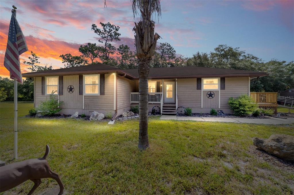 A single-story house with tan siding, a front porch, and an American flag on a pole — 15755 SW 90TH AVENUE, DUNNELLON, FL